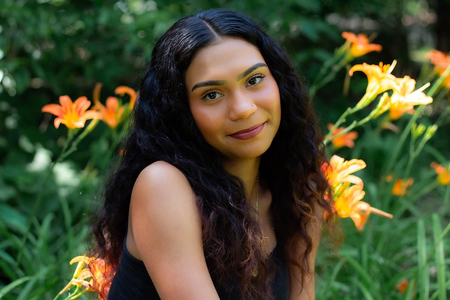 Senior photo of GISH student, Adi Beltran, smiling while sitting in a green field of orange flowers